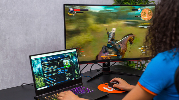 Une fille joue à Witcher sur un ordinateur portable et un écran PC gamer.