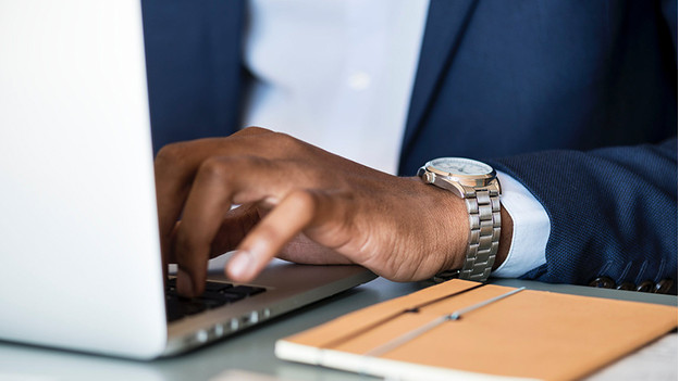 Businessman works on laptop. There's a notebook on the table next to him.