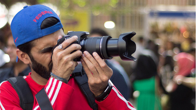 Un homme avec pull rouge et capuchon bleu prend des photos avec l'appareil photo.