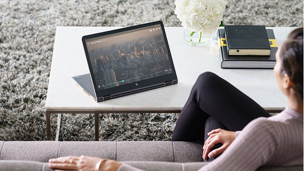 Vrouw kijkt naar serie op laptop in presentatiestand terwijl deze op een tafeltje staat.