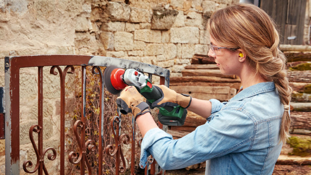 Une femme dérouille une clôture avec une meuleuse d'angle Bosch
