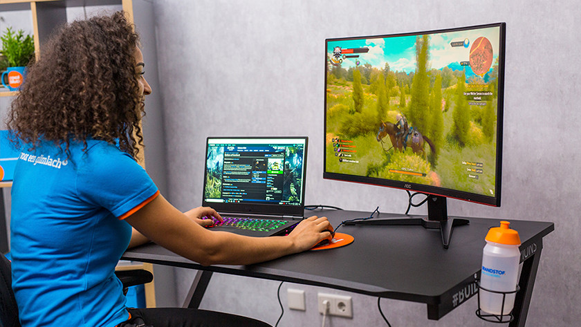 Specialist aan het gamen via een gaming laptop en gaming monitor