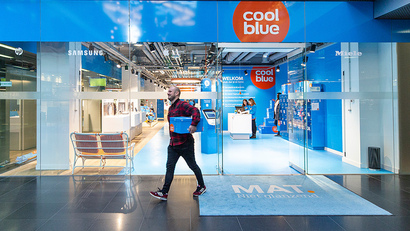 Un homme sort du magasin Coolblue avec une boite Coolblue sous le bras.