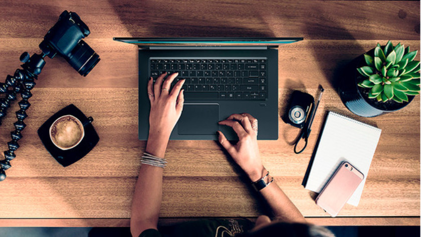 Vrouw werkt op 17 inch laptop met diverse accessoires op het bureau erbij. 