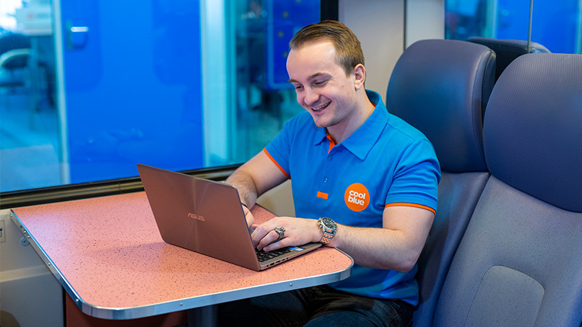 Un homme souriant dans un train travaille sur un ordinateur portable Asus.