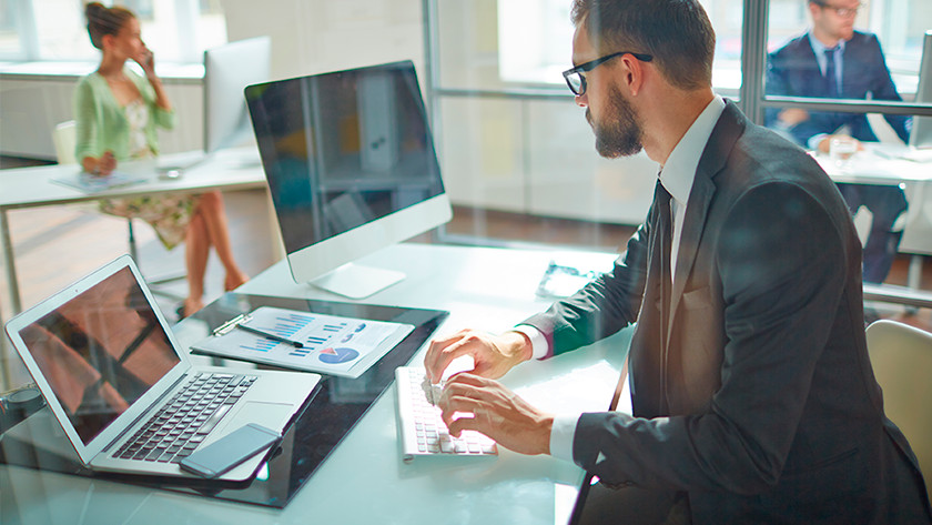 Un homme au bureau travaille avec un ordinateur portable et un clavier.