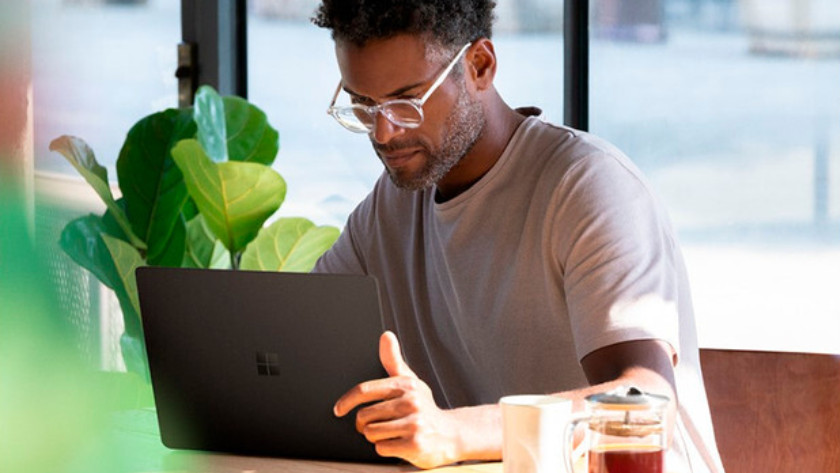 Man werkt op 13 inch laptop in koffiewinkel met plant op de achtergrond. 