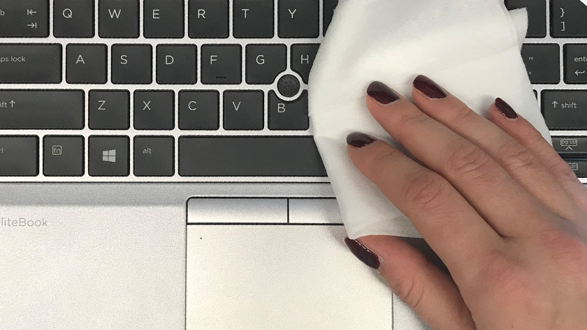 Una mano femenina limpia el teclado HP EliteBook con un paño blanco.