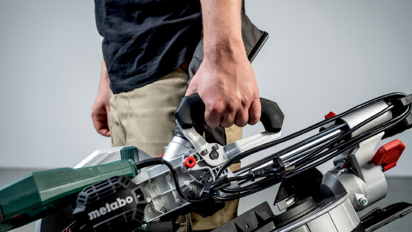 Man tilt de Metabo KGS 254 M afkortzaag met één hand