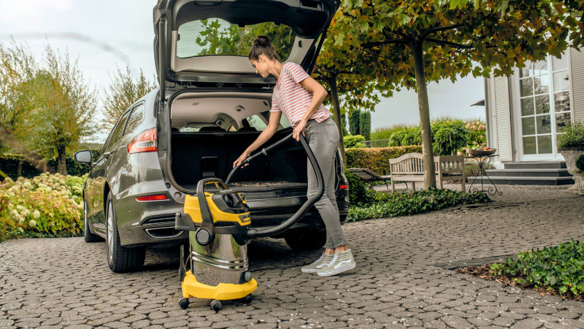 Une femme utilise un aspirateur de chantier Kärcher pour nettoyer sa voiture.