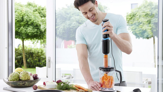 Man snijdt wortel met staafmixer en foodprocessor opzetstuk