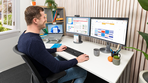 Un homme est assis sur une chaise de bureau, sur le bureau se trouvent 2 écrans PC